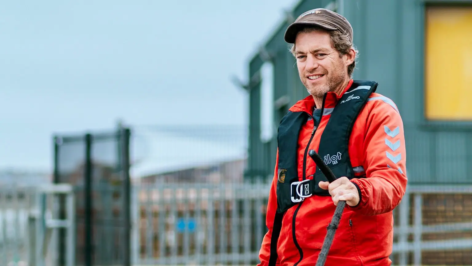 A laughing young woman in a cap and life jacket stands beside a grey-bearded sailor.